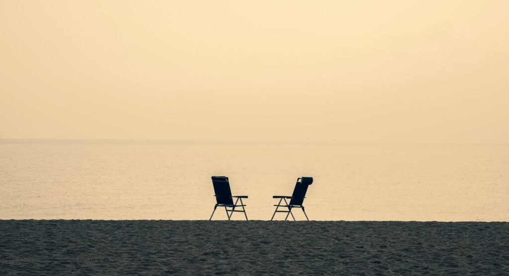 Dos sillas frente al mar en una playa al atardecer.